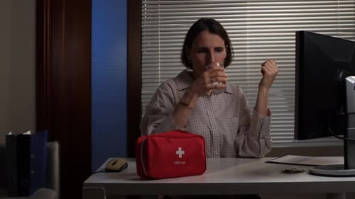 Woman Takes Pill with Water at Desk at Night