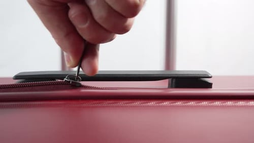 A close-up video shows a hand pulling a single zipper on a red suitcase.