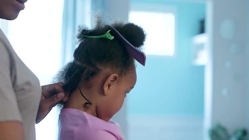 Mid-close up of African American girl getting her hair braided at home during the stay at home ordin