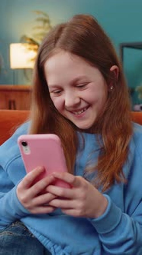 Girl Laughs While Using Smartphone on Couch