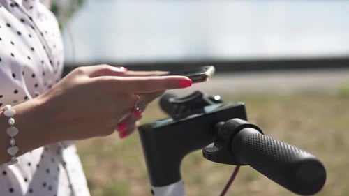 Woman Using Phone Next to Electric Scooter