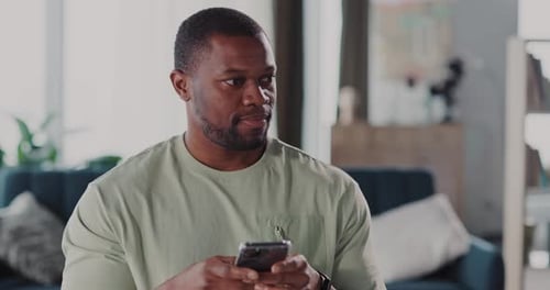 A Man is Engaged in a Mobile Interaction While Seated in His Modern Living Space