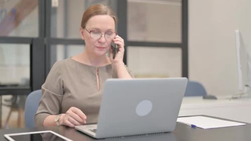 Woman Working at Desk Talking on Smartphone
