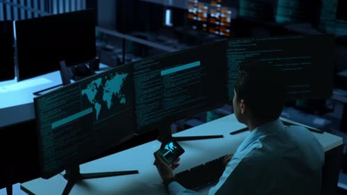 Asian Man Working With Mobile Phone While Write Code With Multiple Computer Screens In office