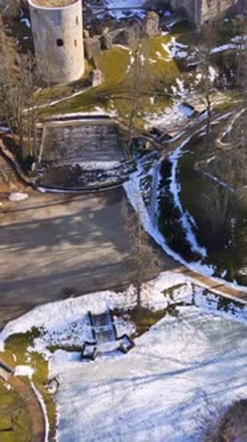 Vertical aerial view of castle park during early spring thaw, showing snowy lawns, curved paths,