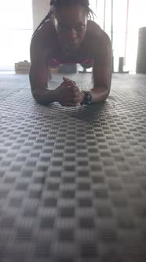 Vertical video: Planking on gym floor, woman focusing on core strength and fitness training