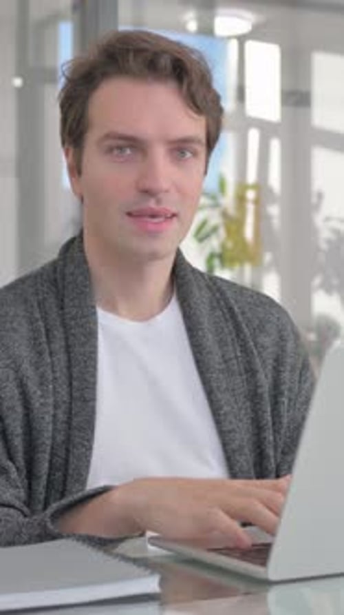 Young Man Smiling at Camera while Working on Laptop in Office, vertical video
