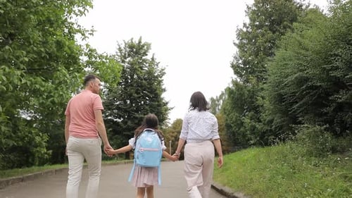 Parents Holding Their Daughter's Hand are Walking in the Summer Park