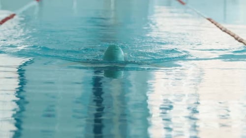 A Young Woman in a Turquoise Swimming Cap Swims in a Breaststroke in the Pool