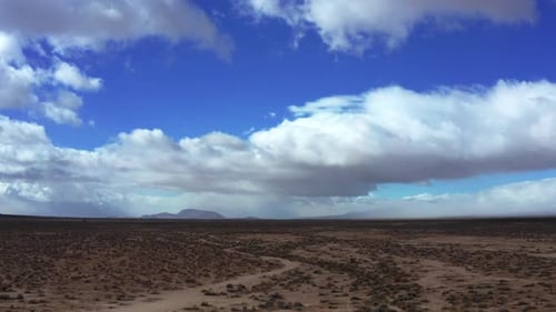 Cumulus clouds watch over the Mojave Desert's rugged landscape - sliding aerial view