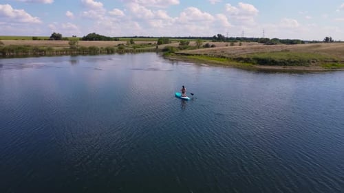 A Young Woman in a Black Bikini Paddling on a SUP Board Over a Tranquil Lake Captured By Drone
