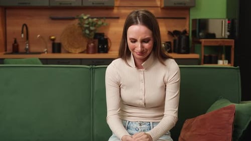 Young Brunette Woman is Crying Sitting Alone on a Green Sofa at Home in the Living Room