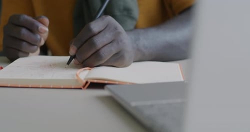 Closeup de mãos escrevendo informações em um caderno enquanto um homem afro-americano estudava em casa