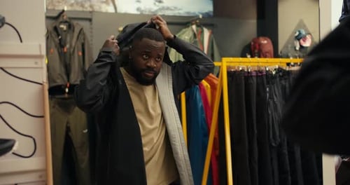 Um afro-americano de estilo explorando o estilo experimentando um blusão preto em uma loja de equipamentos para atividades ao ar livre