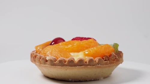 Pasteles giratorios con frutas sobre fondo blanco.