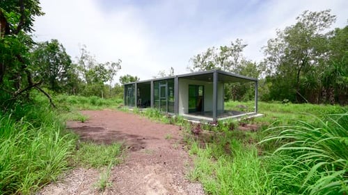 Tropical undeveloped dirt gravel path to demountable rectangular container box style home in
