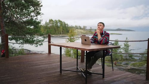 Freelancer With Laptop Sitting Alone On Balcony With Beautiful View On Seascape And Forest