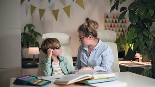 A Mother and Her Son are Sitting at a Table Doing School Homework Together