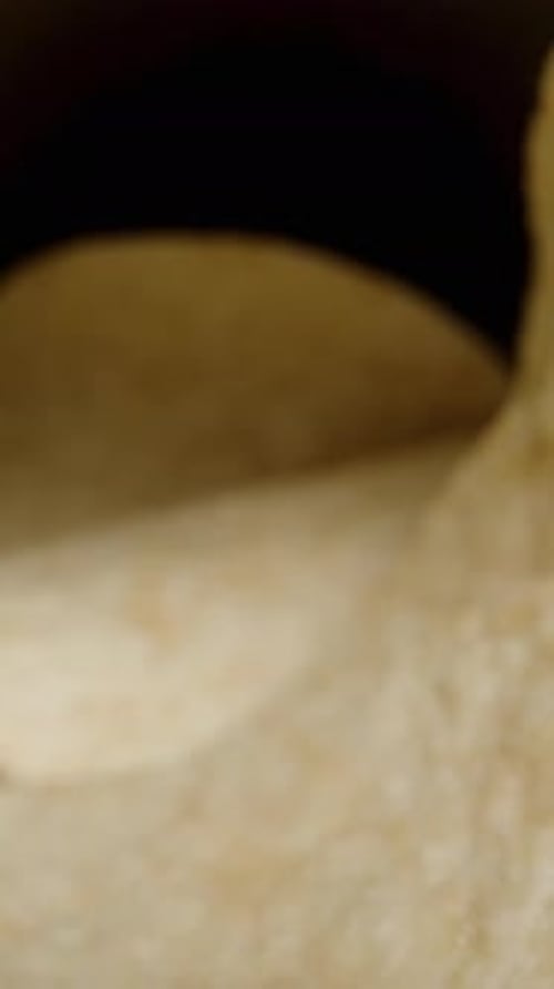 Vertical video. Corn chips, hyperbolic paraboloid in shape, are scattered from a can onto the table