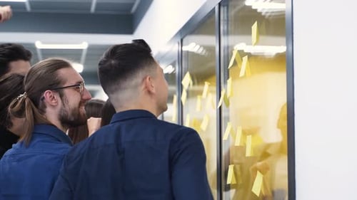 Business Team Brainstorm Writing Ideas on Paper Sticker Notes and Post It on Glass Wall Startup