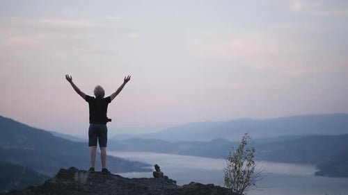 Hiker stands with arms raised on mountaintop with beautiful sunset view