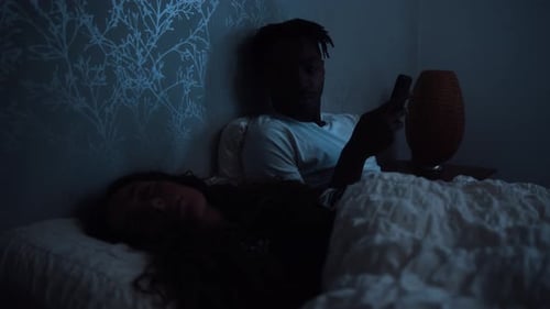 Un homme regarde son partenaire tout en regardant un téléphone intelligent en restant éveillé tard dans la nuit