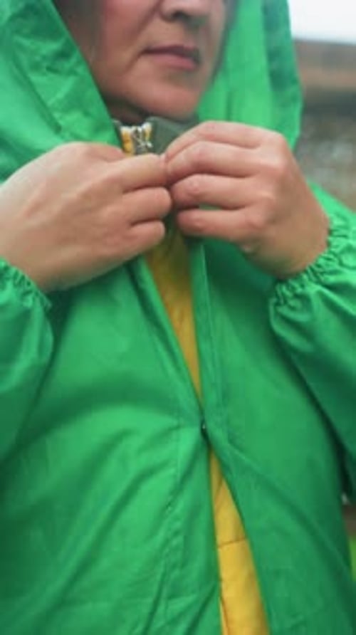 Closeup of Woman Buttoning Green Raincoat Near Swing Bench in Outdoor Setting
