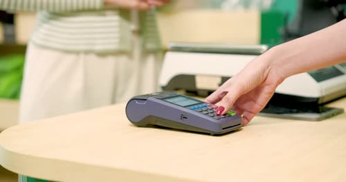 Asian female customer tapping credit card on contactless terminal to pay for purchase at modern