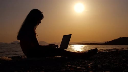 Silhouette of Woman on Beach Working at Sunset