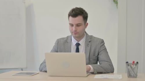 Young Businessman Celebrating Online Success on Laptop in Office