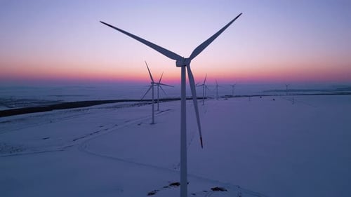 Aerial View of a Wind Farm in a Snowy Landscape at Sunset Large Wind Turbines Stand Tall Against the
