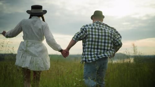Couple Holding Hands and Running Through a Grassy Field at Sunset