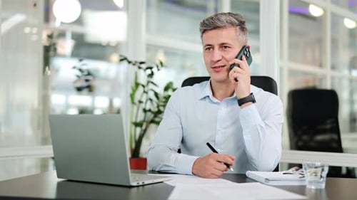 Professional Businessman Engaged in a Productive Phone Call and Taking Notes in a Modern Office
