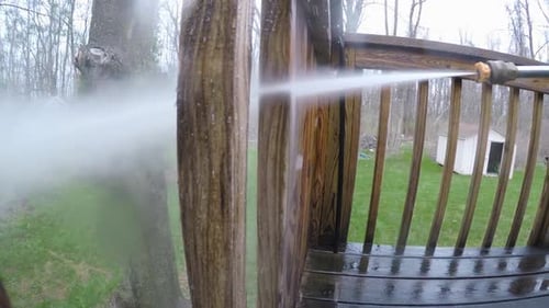 A man uses a power washer to clean a wooden deck railing post. in 1080p slow motion
