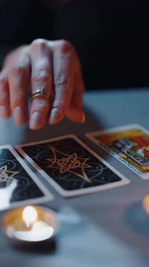 Gros plan de la main plaçant des cartes de tarot sur la table avec des bougies allumées