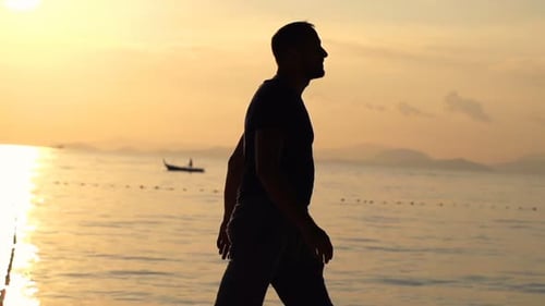 Man silhouette walking on golden beach at sunset in super slow motion