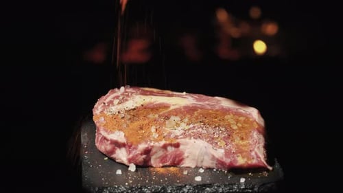 A rotating piece of steak on the background of fire. Sprinkle with paprika