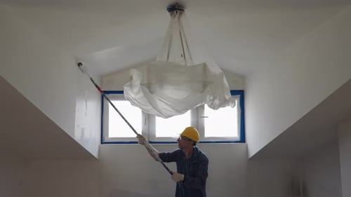 A Man Paints a Wall with a Roller Makes Repairs in the Room of the Attic Floor
