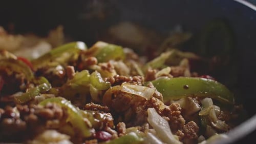 Pouring sauce in homemade mexican food and mixing it all with a wooden spoon, close up view.