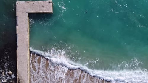 Aerial drone top view at stone pier breakwater, turquoise water in sea, beach with brown sand is emt