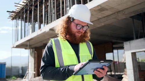 Bearded construction engineer typing notes on tablet while inspection construction site