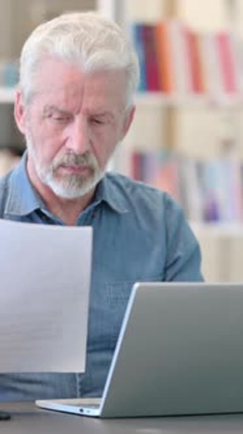 Senior Man Reviewing Documents with Laptop Indoors