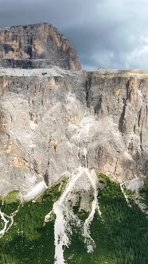 Drohnenaufnahme einer massiven senkrechten Kalksteinfelse, die sich über dichtem Alpenwald erhebt. Die Imposi