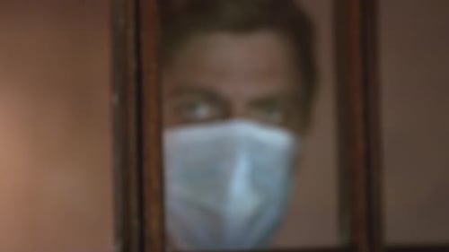 Adult wearing medical face mask looking out window