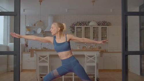 Active Sporty Fitness Senior Woman Stretching in Yoga Warrior Two Pose Indoors