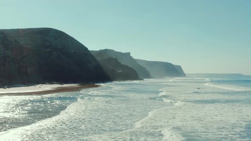 Breathtaking aerial view of coastline and cliffs. The sea is making waves for surfing.