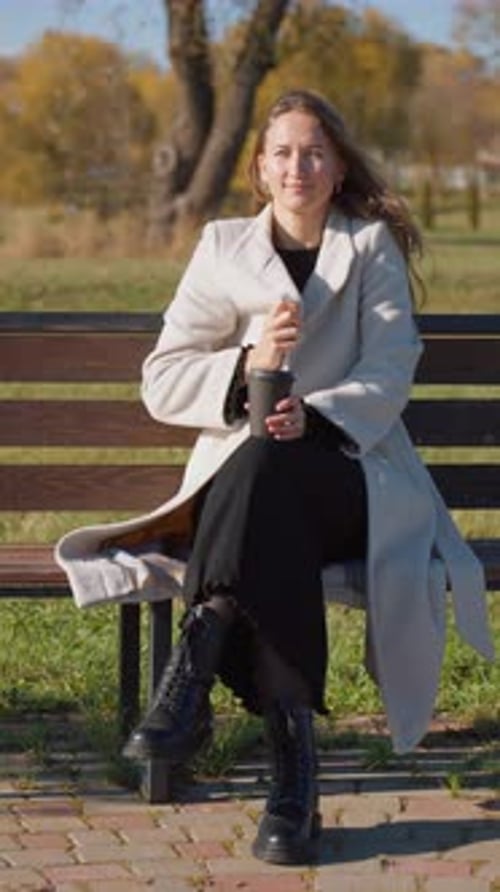 Stylish Woman Relaxing on Park Bench With Coffee