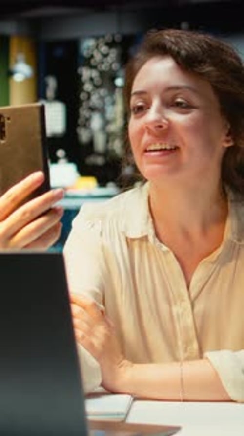 Vertical Video Entrepreneur Takes Part in a Virtual Briefing at Her Workstation with Phone