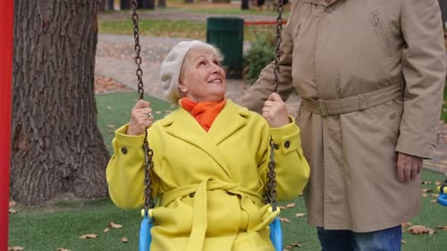 Front View Happy Carefree Senior Woman Enjoying Leisure As Unrecognizable Man Pushing Swings on