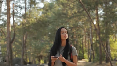 Brunette Female Hiker Navigates with Smartphone in a Lush Forest